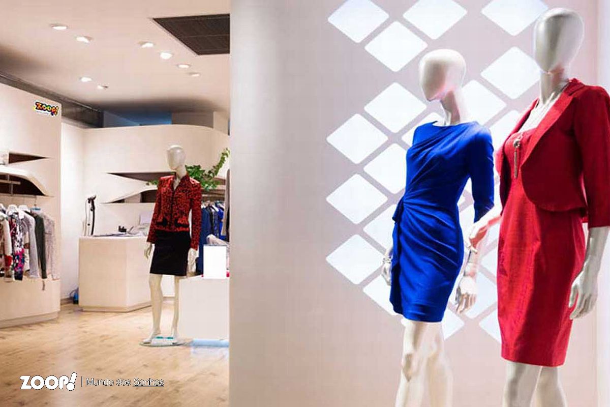 Sonhar com roupa nova. Dois manequins vestidos com vestidos azule e outro vermelho, na entrada de uma loja.