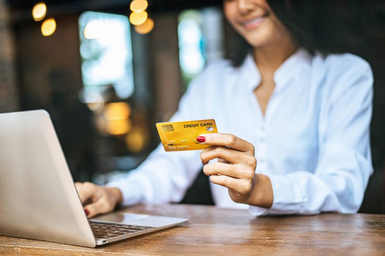 Uma mulher jovem usando um cartão de crédito enquanto faz uma compra pela internet.